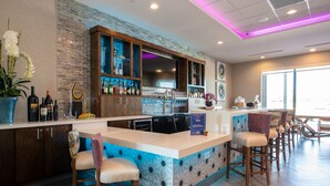 A bar area with a counter, stools, and a variety of bottles and glasses. - Home2 Suites by Hilton Wichita Northeast (Wichita)