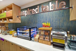 A breakfast buffet area with various food items, a sign reading "inspired table," and a coffee machine. - Home2 Suites by Hilton Wichita Northeast (Wichita)