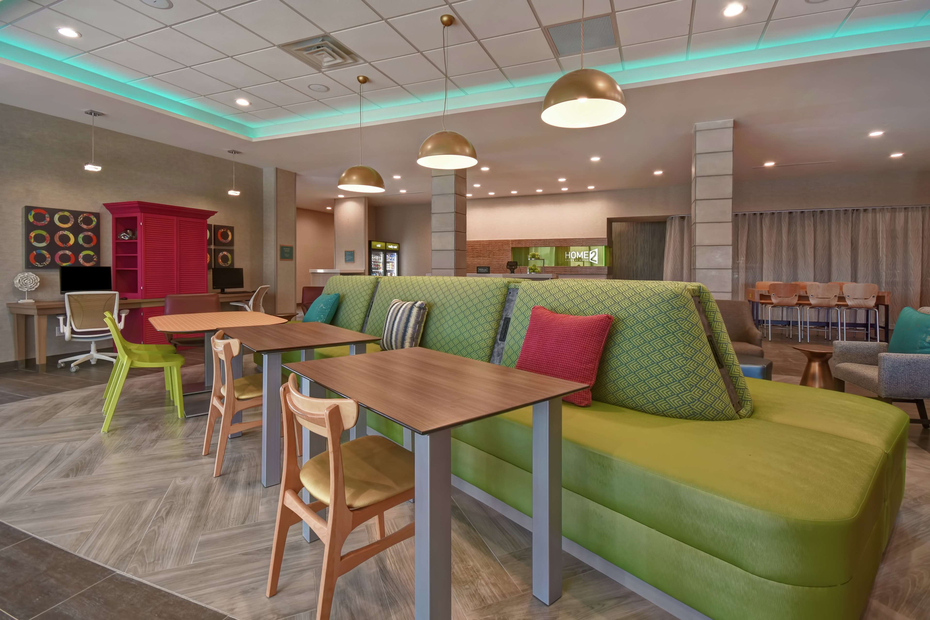 A modern hotel lobby with a green sofa, wooden tables, and chairs.