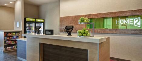 A hotel reception area with a counter, vending machines, and a display of green apples.