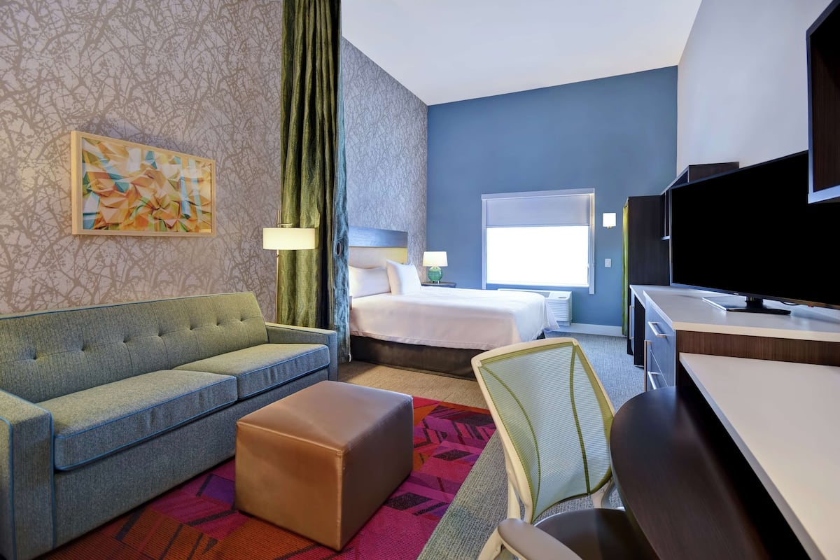 A hotel room with a sofa, a bed, a desk, a television, and a painting on the wall.