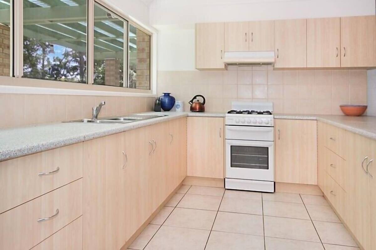 Una cocina compacta con armarios de madera clara, estufa a gas, horno empotrado y ventana que proporciona luz natural.