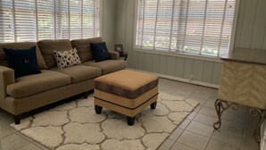 A living room with a beige sofa, patterned cushions, a leopard print ottoman, and a small side table.
