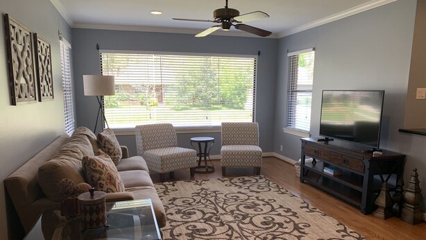 A living room with a sofa, two armchairs, a coffee table, a TV, and a ceiling fan.