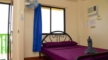 A single bed with a purple mattress, a blue curtain, a wall-mounted fan, and a no-smoking sign.