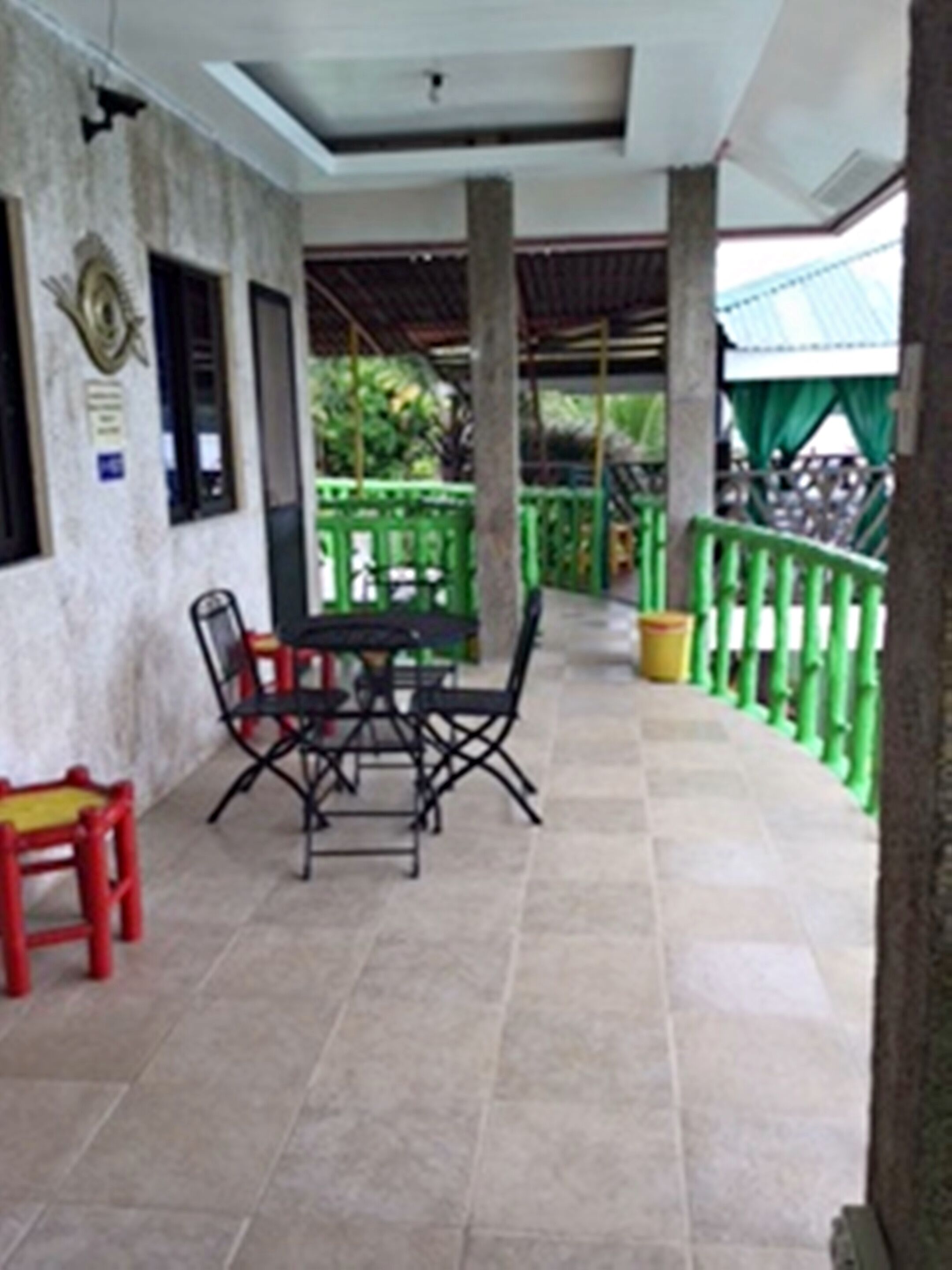 A covered outdoor area with a table and chairs, a small red bench, and a green railing.