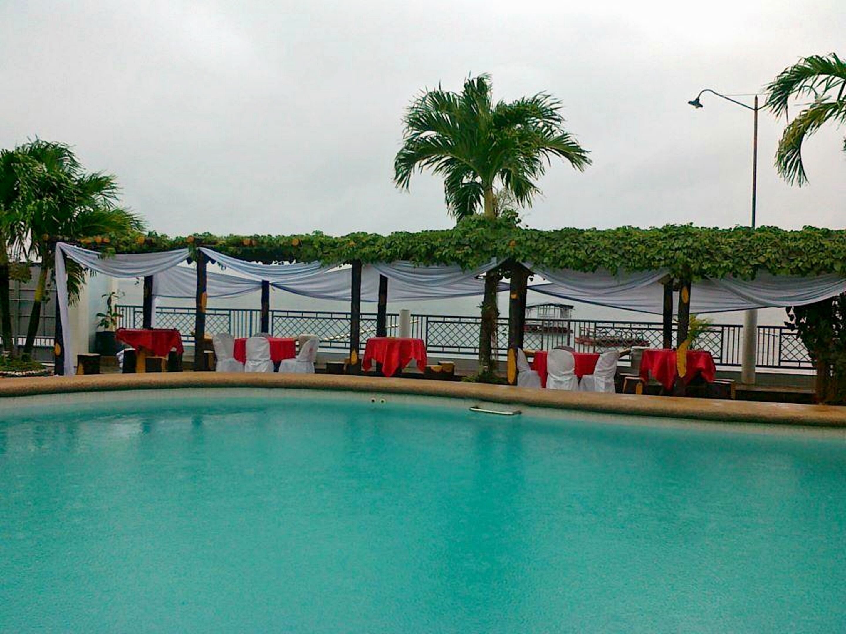 A pool area with covered seating and palm trees.