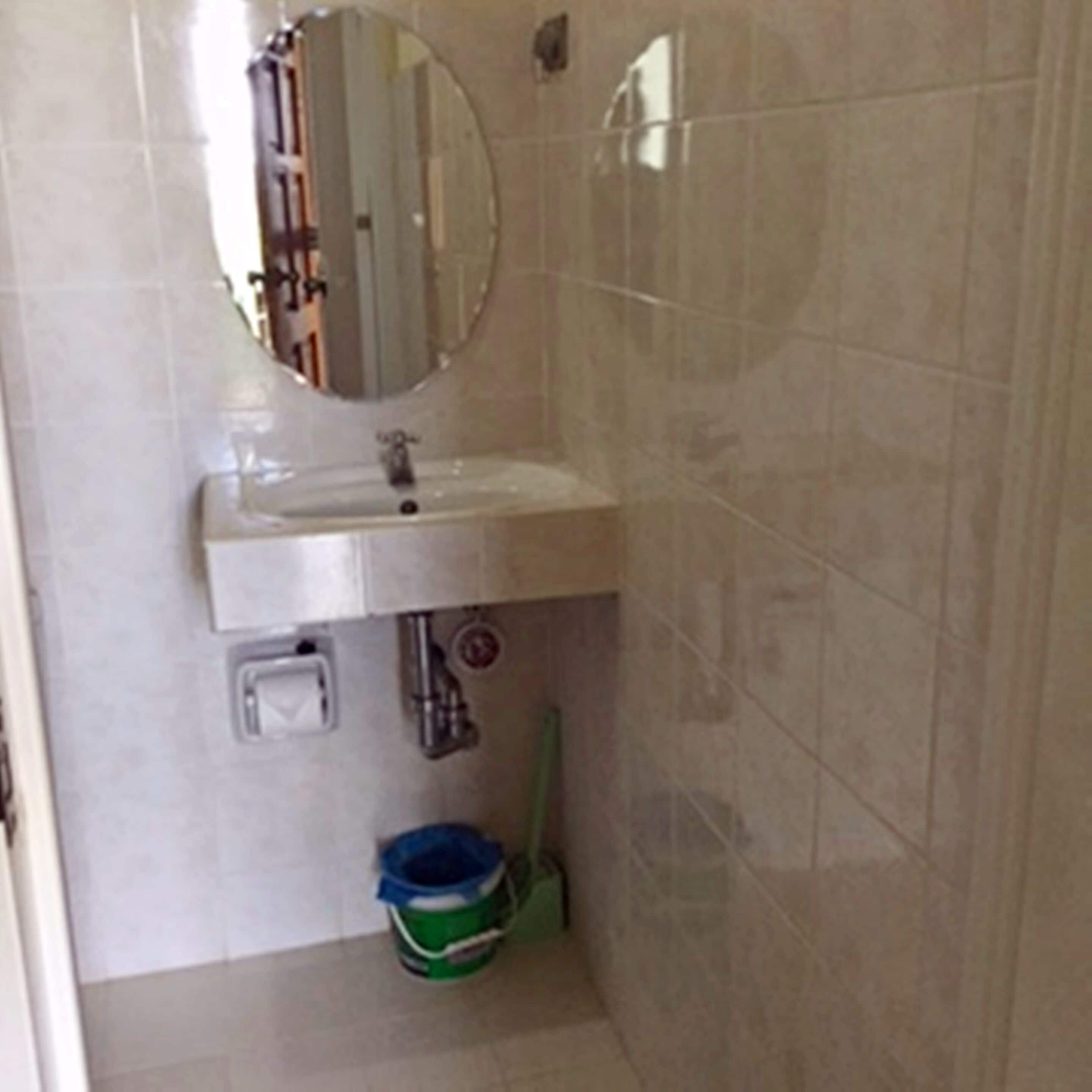 Un baño con un lavabo blanco, un espejo encima y un cubo verde en el suelo.
