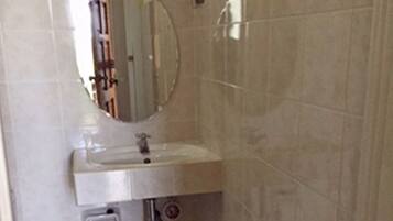 Un baño con un lavabo blanco, un espejo encima y un cubo verde en el suelo.
