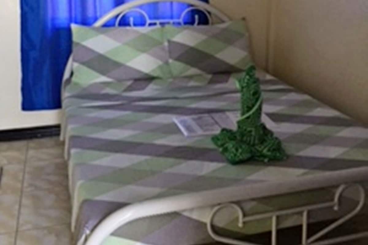 A single bed with a metal frame, a blue curtain, and a wall-mounted air conditioning unit.