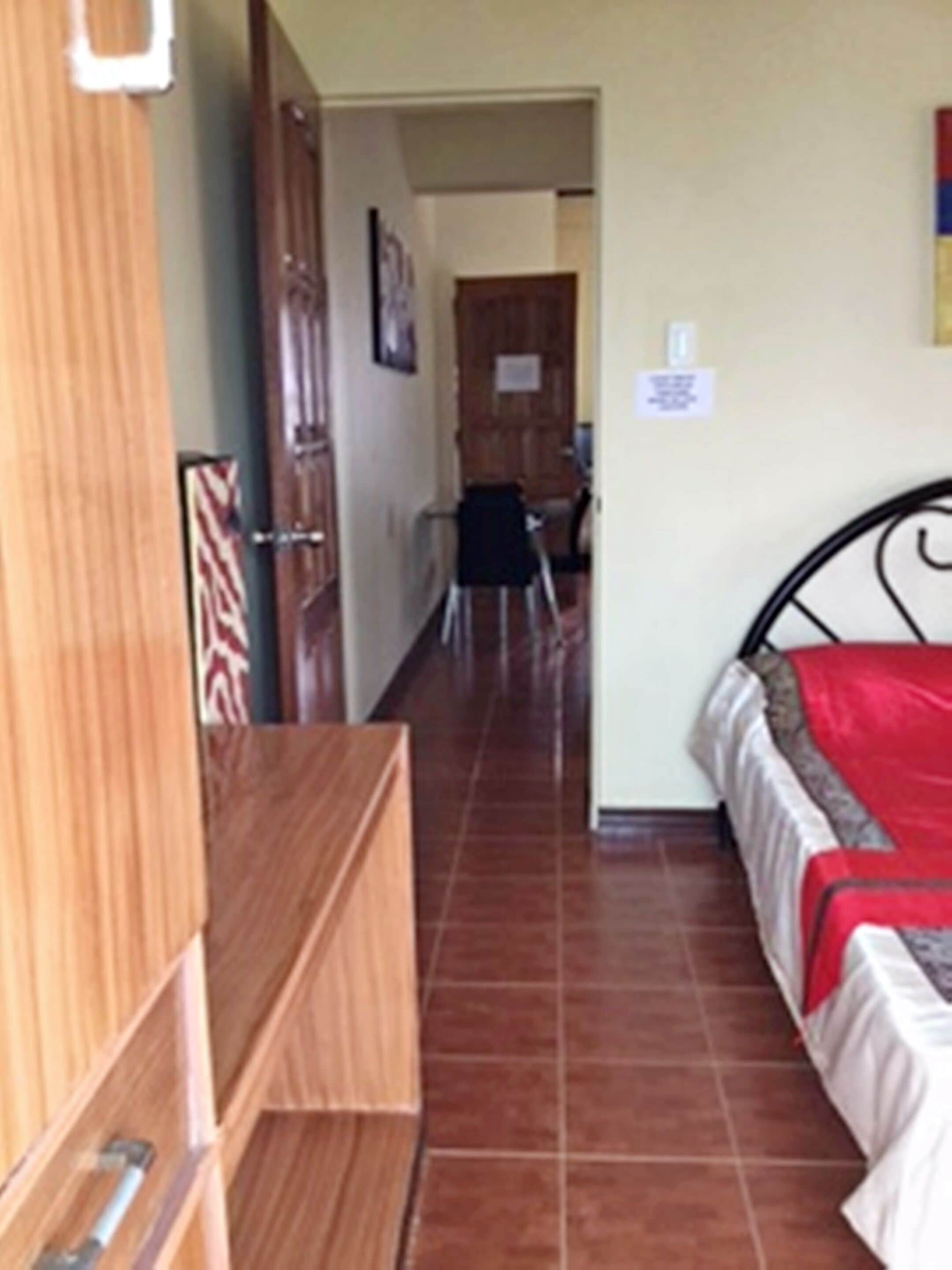 Un dormitorio con un armario de madera, una cama con una colcha roja y un suelo de baldosas.