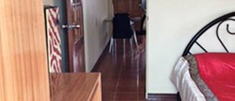 Un dormitorio con un armario de madera, una cama con una colcha roja y un suelo de baldosas.