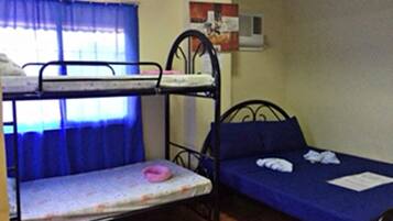 Habitación tipo dormitorio con literas, una cama individual, una ventana con cortinas azules y un aire acondicionado de pared.