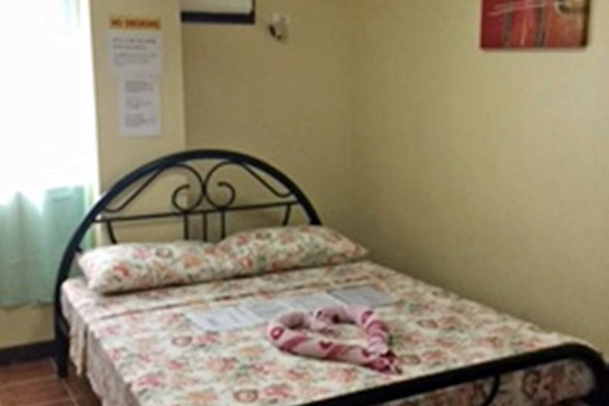 A single bed with floral bedding, a nightstand, a wall-mounted air conditioner, and a red abstract painting.