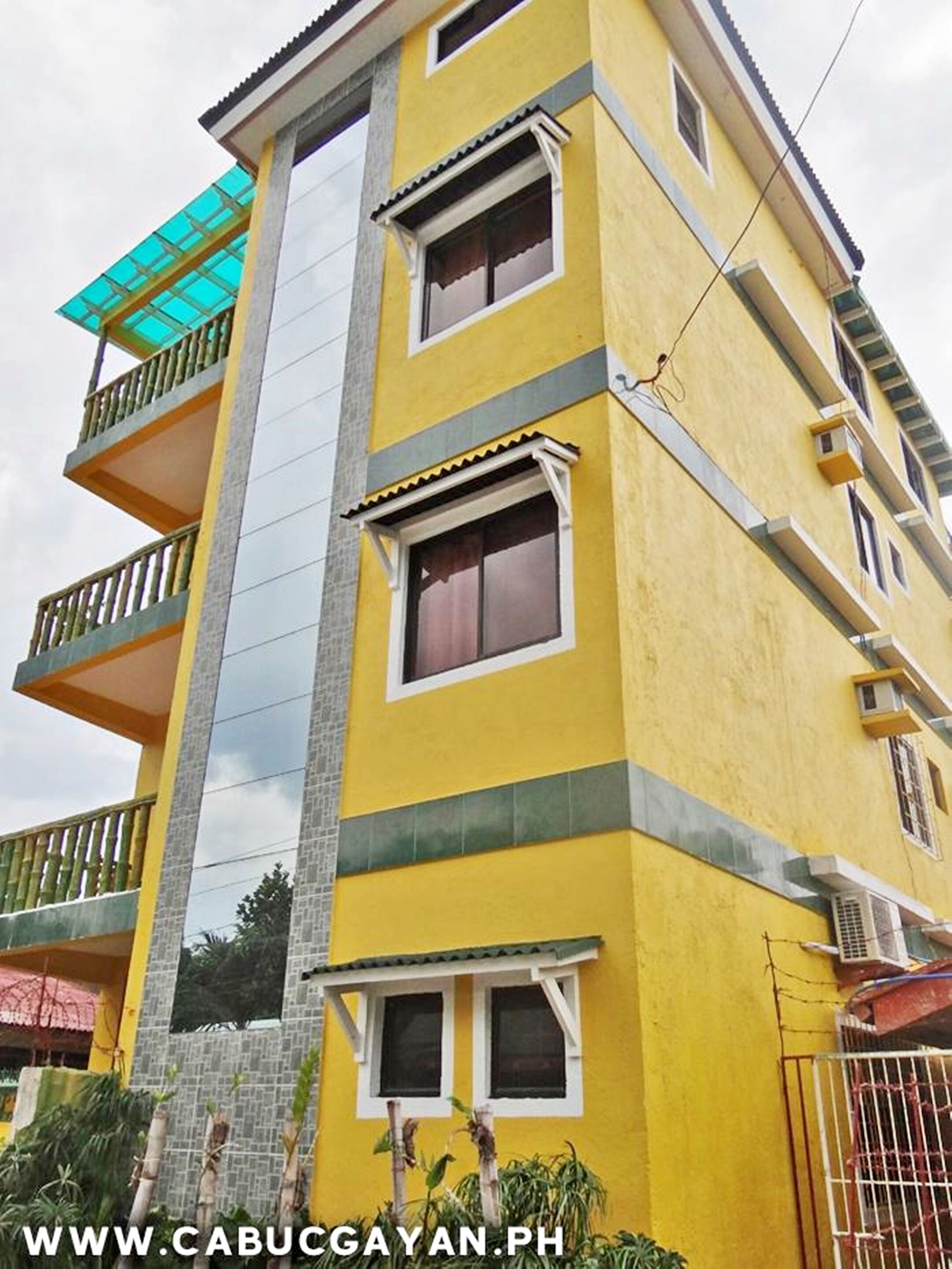 A multi-story yellow building with balconies, windows, and a visible air conditioning unit.
