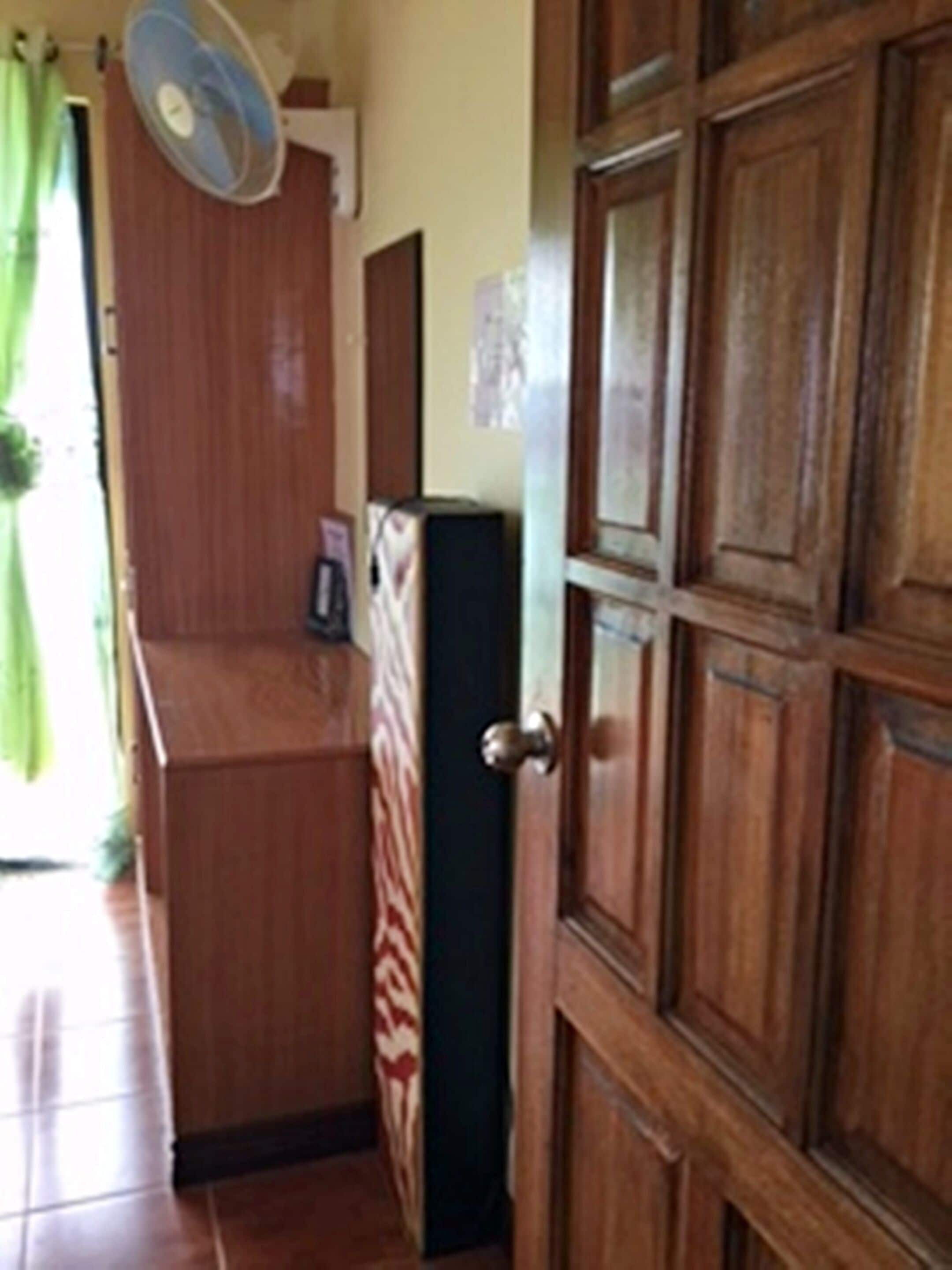 A wooden door with a glass panel, a small fan mounted on the wall, and a refrigerator in the background.