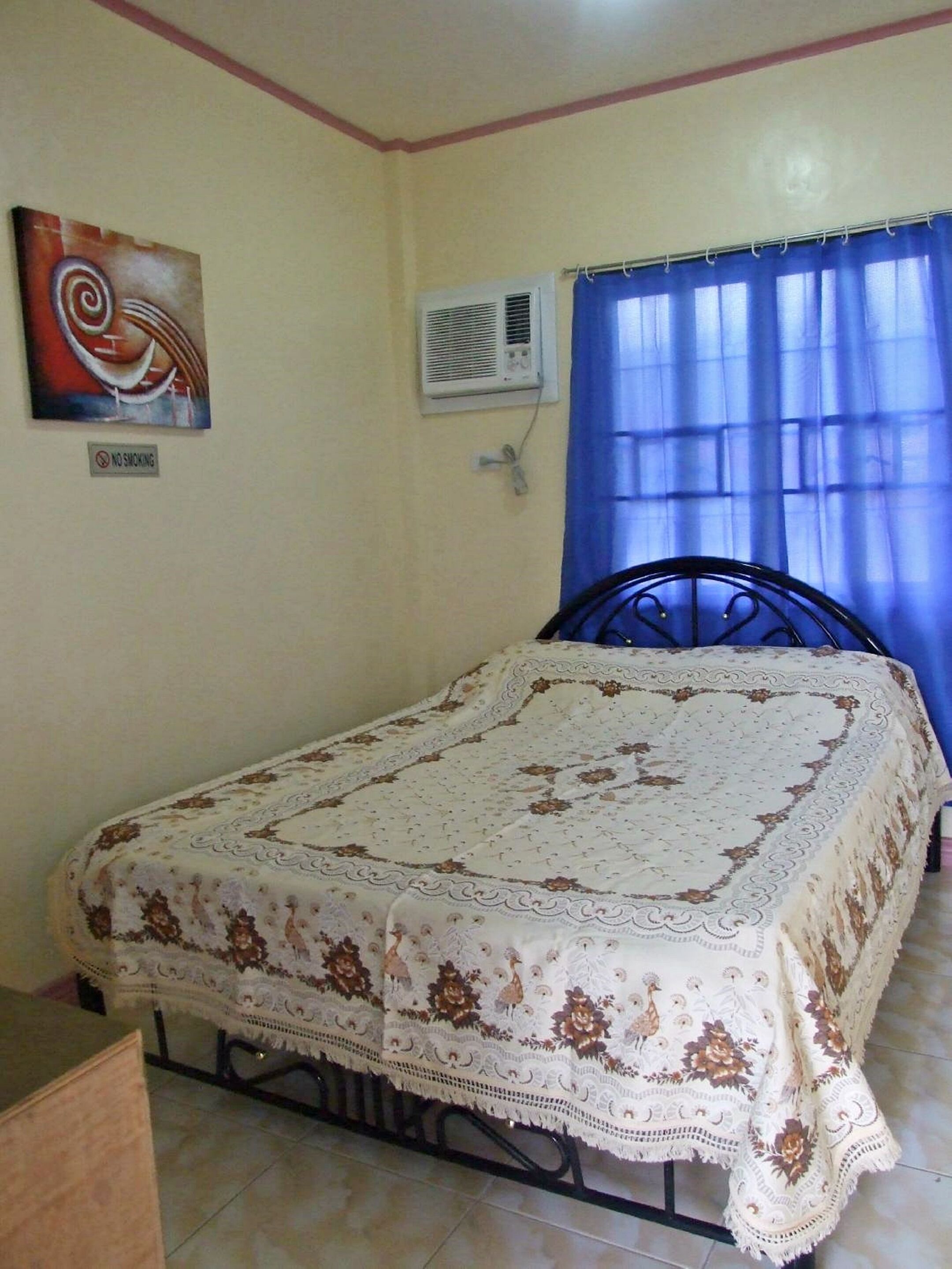 Una camera da letto con un letto, un condizionatore d'aria a parete, un cartello con scritto 'No Smoking' e una finestra con tende blu.
