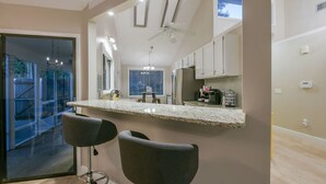 Una cucina moderna con un piano di lavoro in marmo, due sgabelli da bar e una ventola a soffitto.