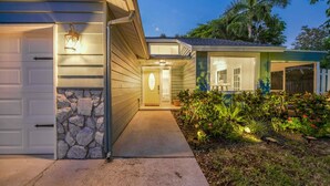 Una casa residenziale con un muro in pietra decorativo, un garage e un cortile anteriore ben illuminato con piante.