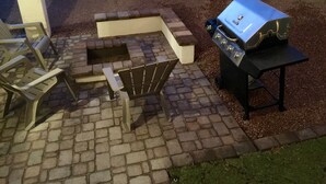 Une terrasse extérieure équipée d’un barbecue, de chaises et d’un foyer.