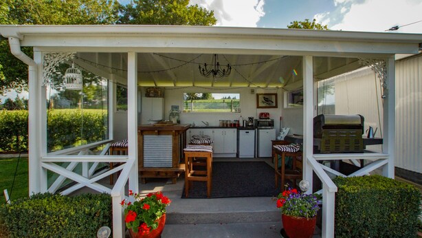 A covered outdoor kitchen area with a dining table and chairs, surrounded by potted plants.