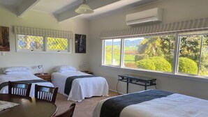 A hotel room with two beds, a dining table, and a view of a garden.