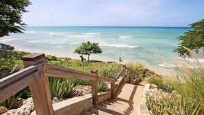 A wooden staircase leading to a beach with clear turquoise water and a view of the ocean.