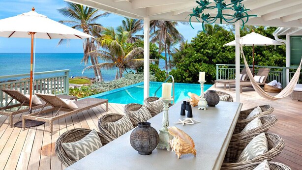 A covered outdoor area with a pool, lounge chairs, and a view of the ocean.