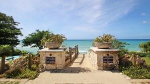 A pathway leading to a beach with two signs reading "Cotton Bay Sea Window" and "Project of the Scenic Barbados Trust and Tourism Development Corp."