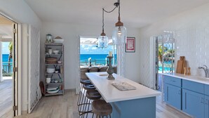 A kitchen with a view of the ocean, a bar area with stools, and a dining table.