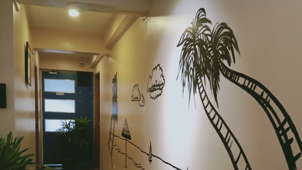 Un pasillo con suelo de madera, una pared con un mural de palmeras y una puerta al final.