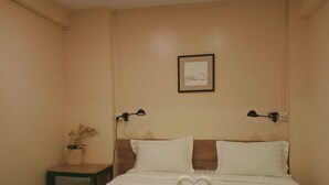 Habitación de hotel con una cama, dos lámparas de noche, un cuadro en la pared y una pequeña mesa con una planta.