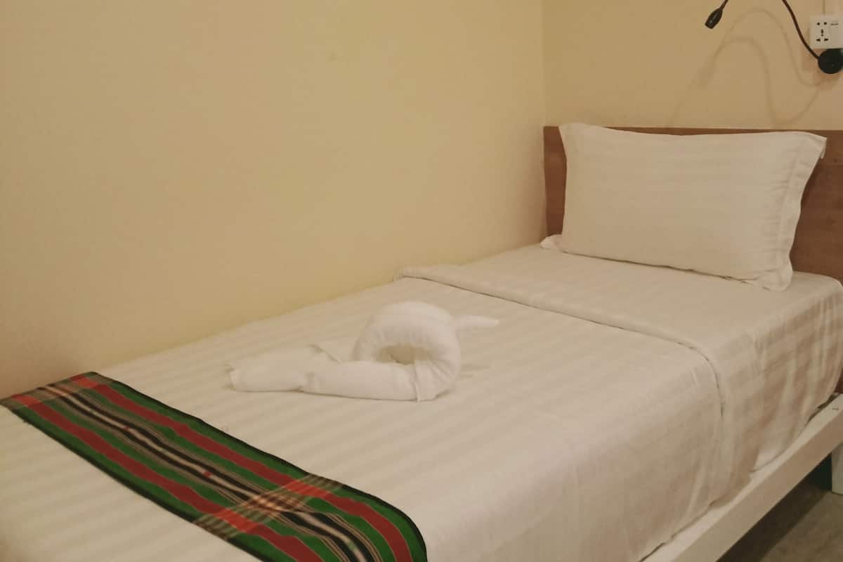 A single bed with white bedding, a striped blanket, and a wall-mounted lamp.