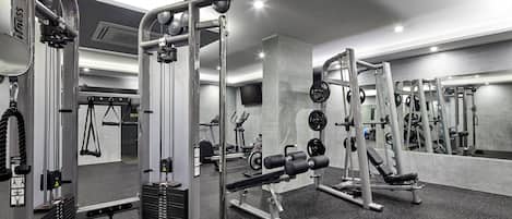 A gym with various exercise equipment, including weight machines and free weights, and a mirrored wall.