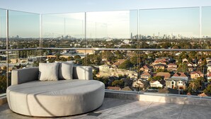 A modern living room with a curved sofa and a panoramic city view through floor-to-ceiling glass walls. - Crowne Plaza Sydney Burwood by IHG (Burwood)