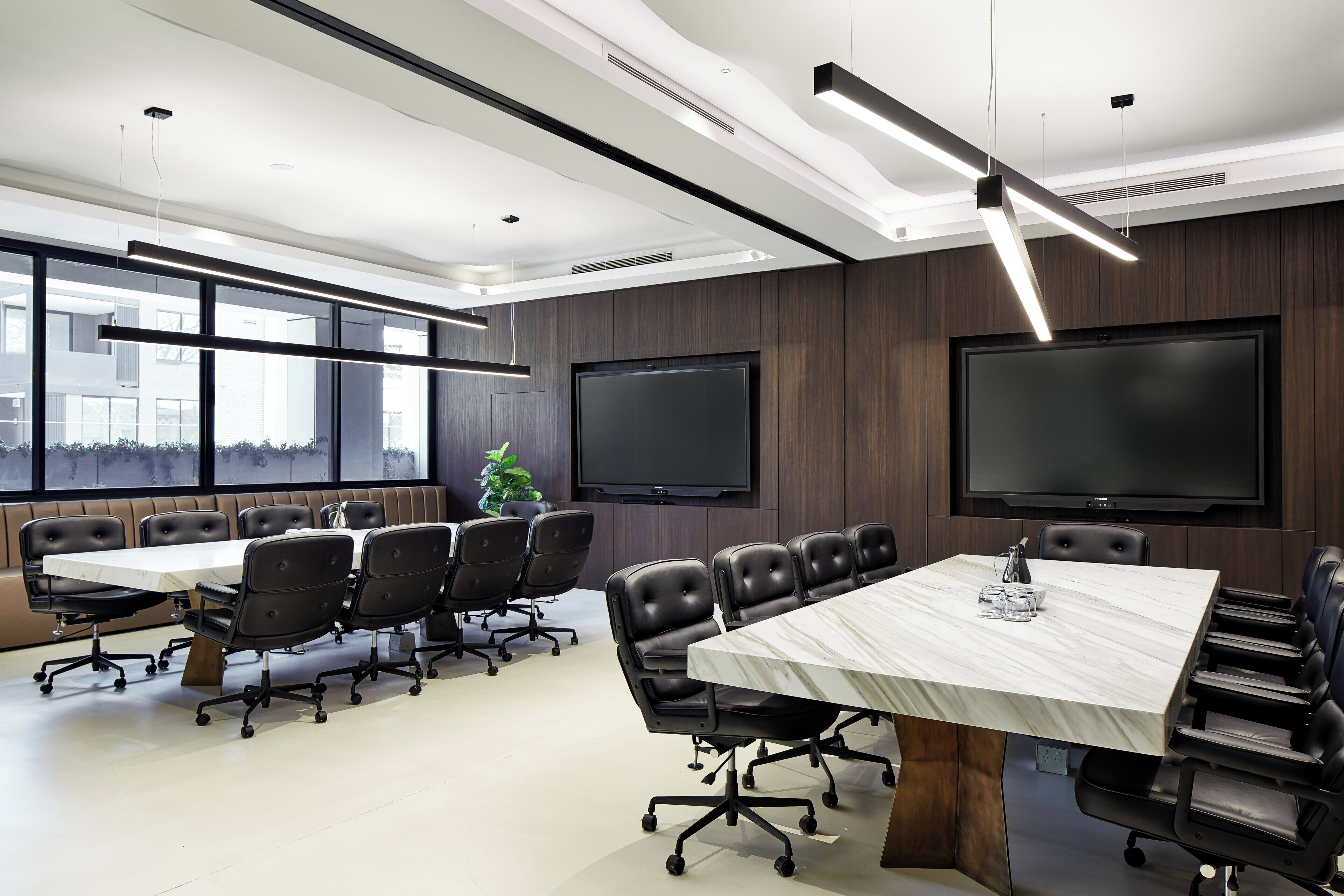 A modern conference room with a large table, black leather chairs, a large screen, and a city view through the windows.