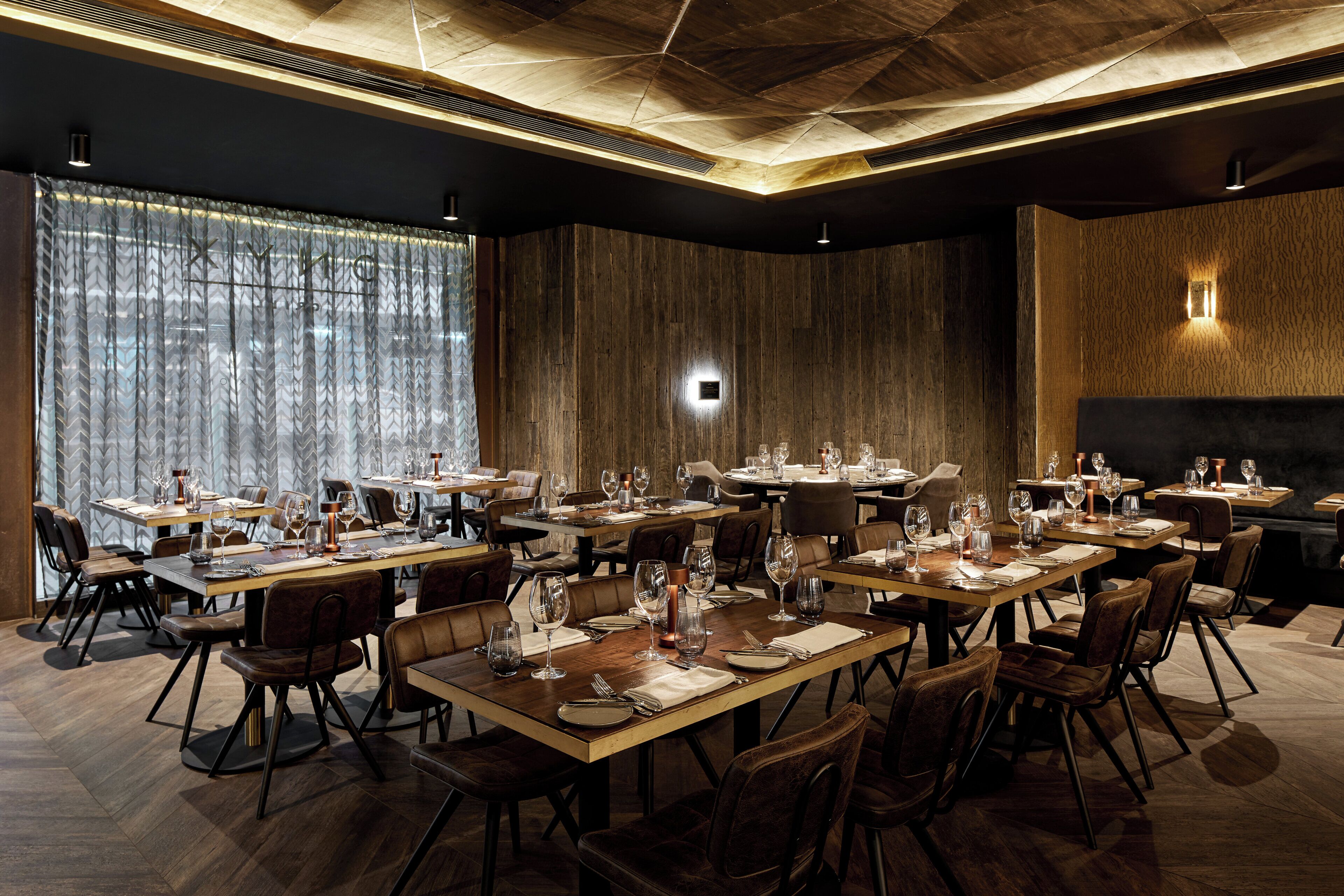A restaurant with multiple dining tables, chairs, and a large window with curtains.