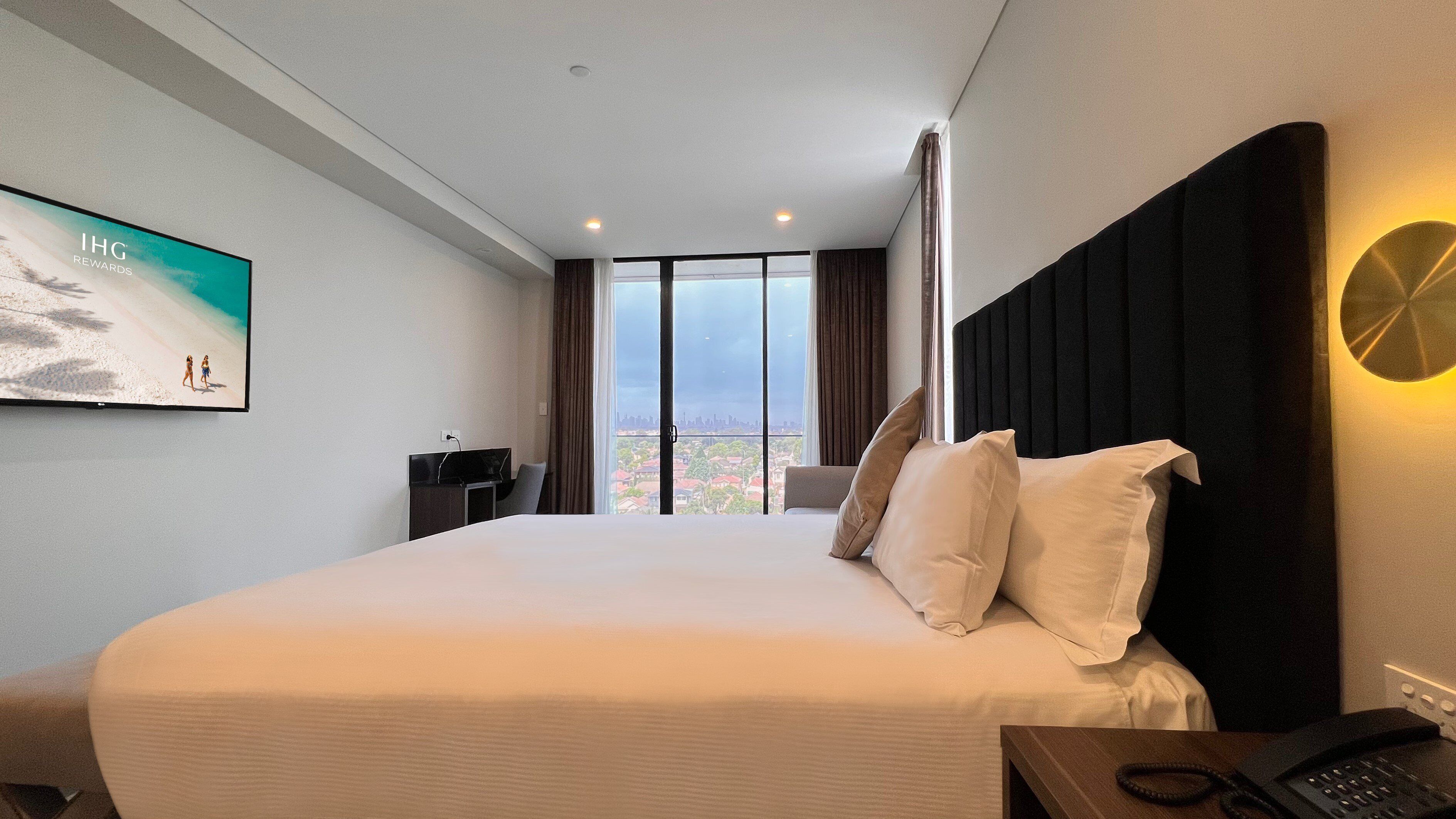 A hotel room with a bed, a desk, a chair, a TV, and a view of the city.