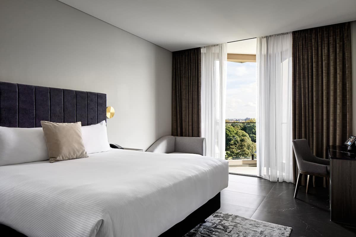 A modern hotel room with a large bed, a desk, and a view of the outdoors.