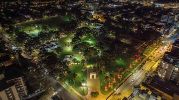 An aerial view of a cityscape at night with illuminated streets, a park with green lighting, and buildings surrounding the area.