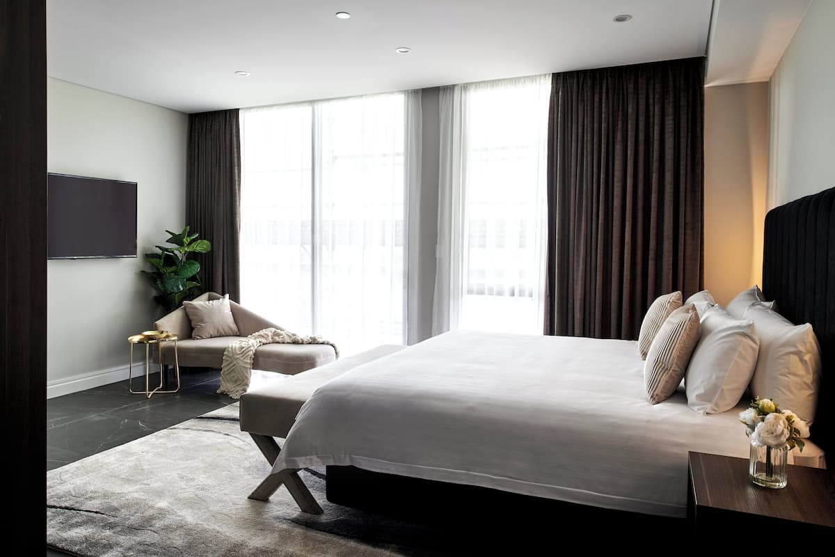 A modern bedroom with a large bed, a sofa, a TV, and a large window with curtains.
