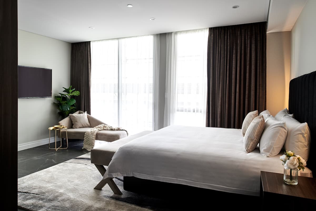 A modern bedroom with a large bed, a sofa, a TV, and a large window with curtains.