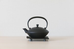 A black teapot on a stand.