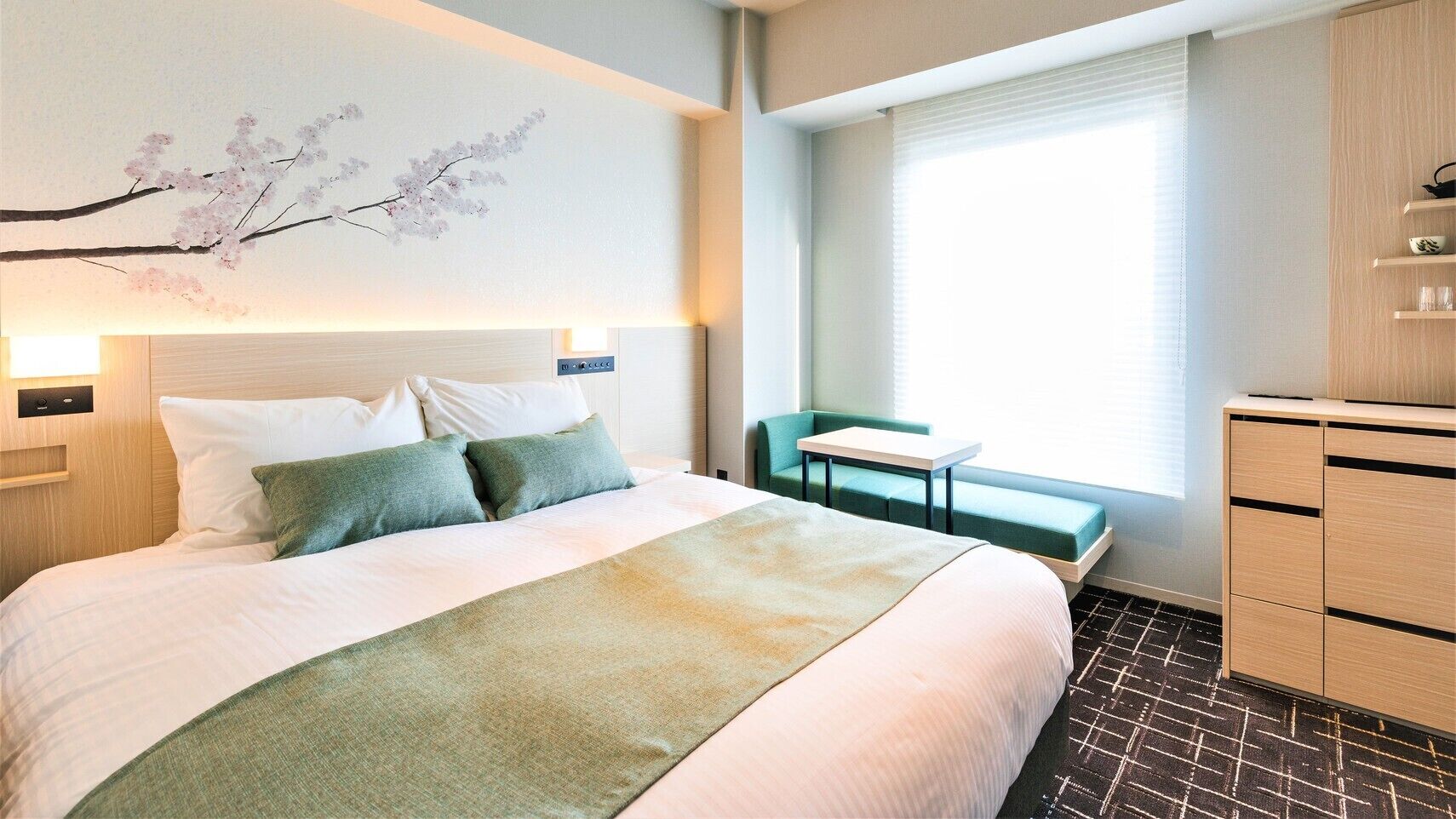Une chambre d’hôtel avec un lit, une petite table, un banc et une armoire.