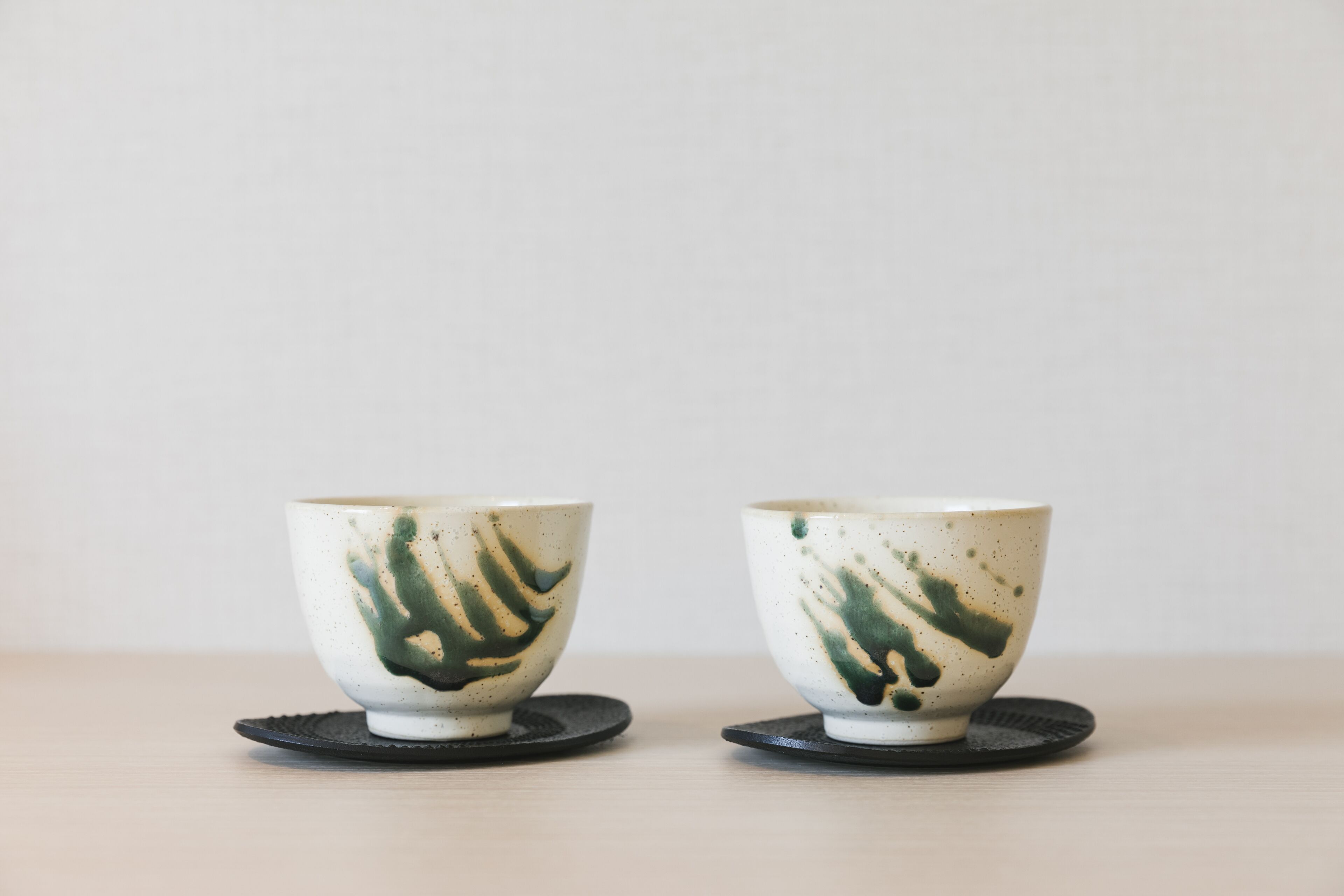 Two ceramic cups with green designs on a light-colored surface.
