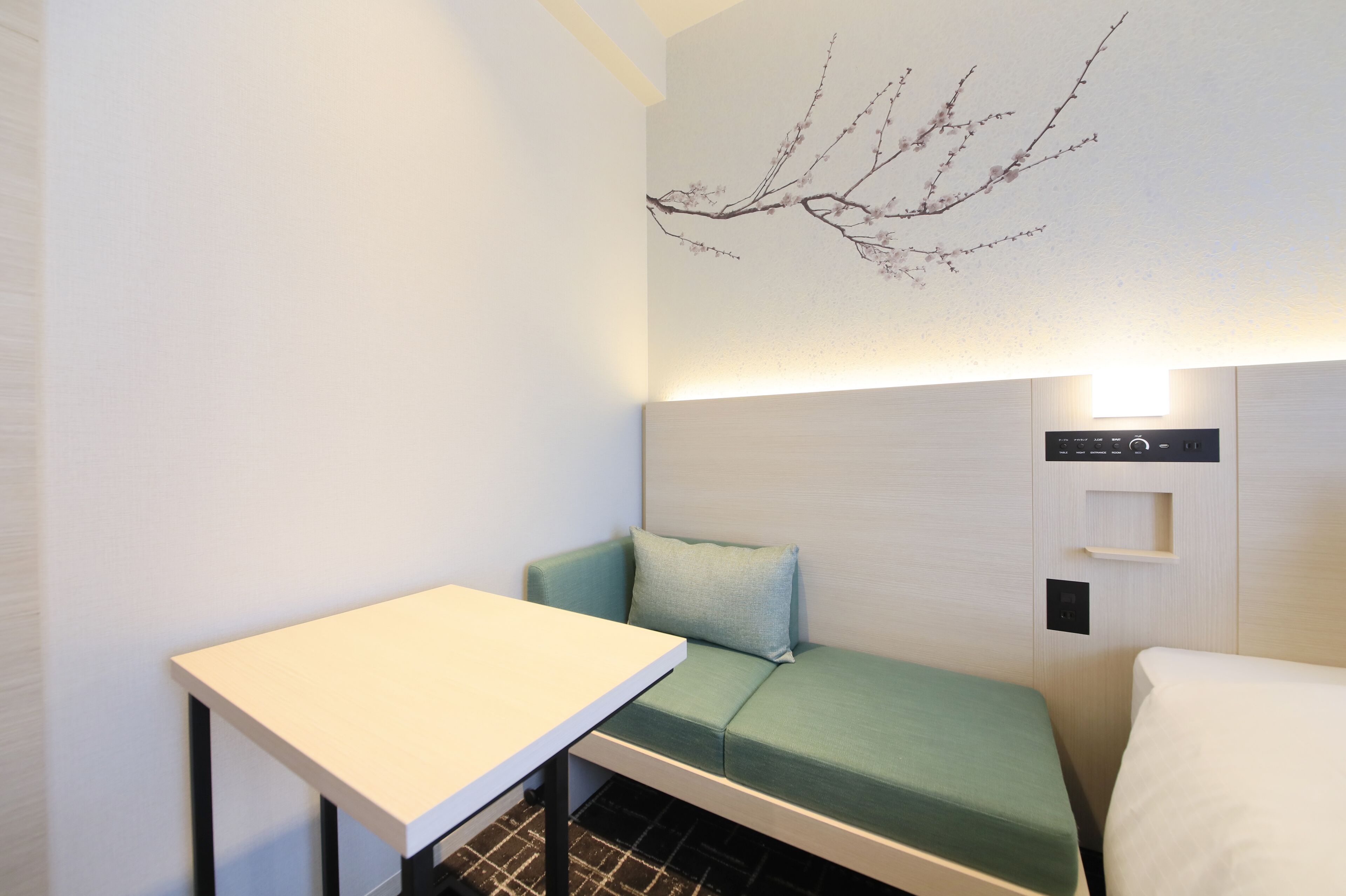Une petite chambre moderne, équipée d’un lit, d’un canapé, d’une table et d’un luminaire fixé au mur.