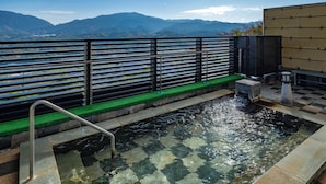 Un área de aguas termales con vistas a montañas, una cerca de madera y un sendero de piedra que lleva al agua.