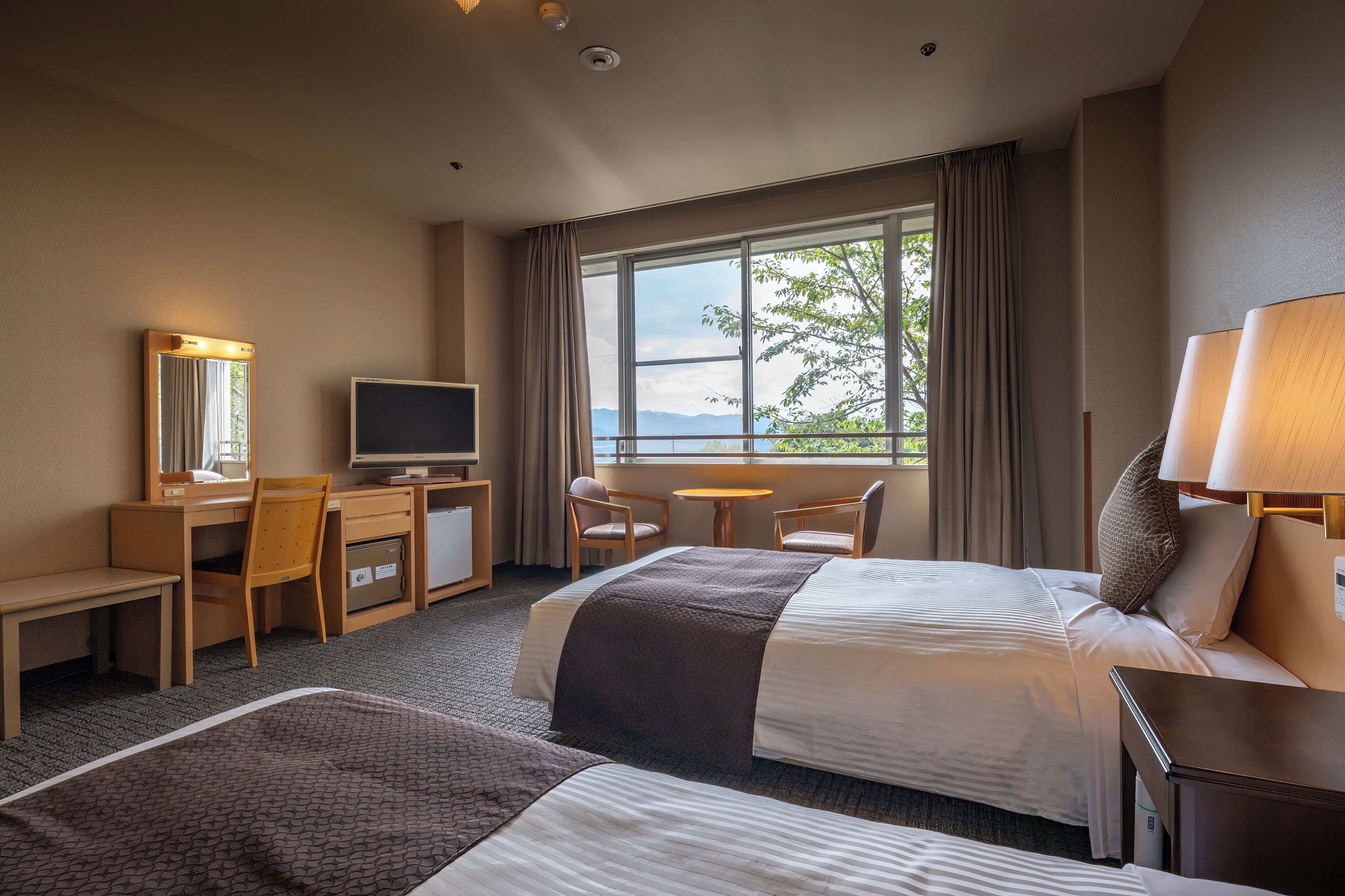 Quarto de hotel com cama, escrivaninha, cadeira, televisão e janela com vista.