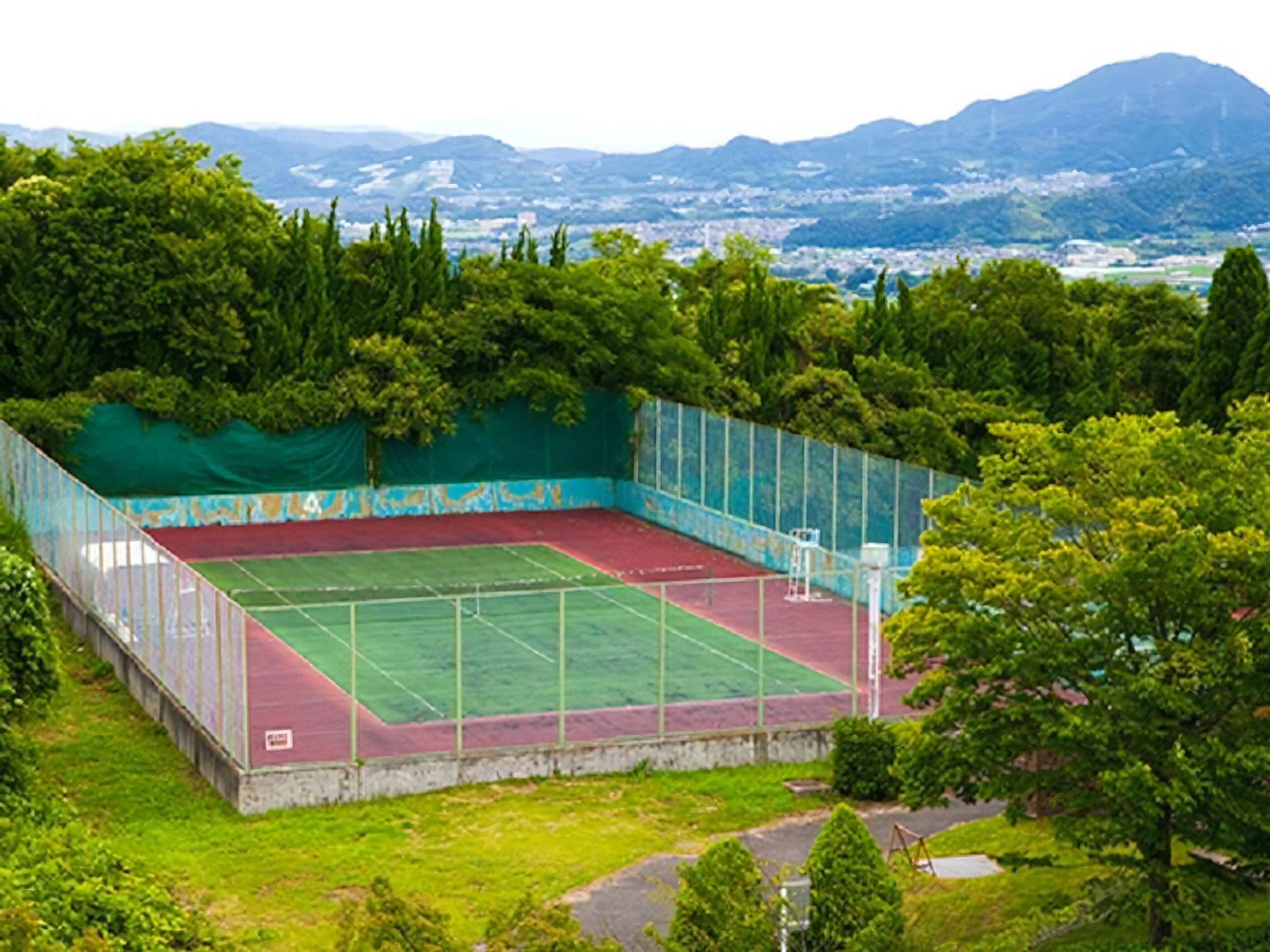A tennis court surrounded by trees and a view of a cityscape in the background.