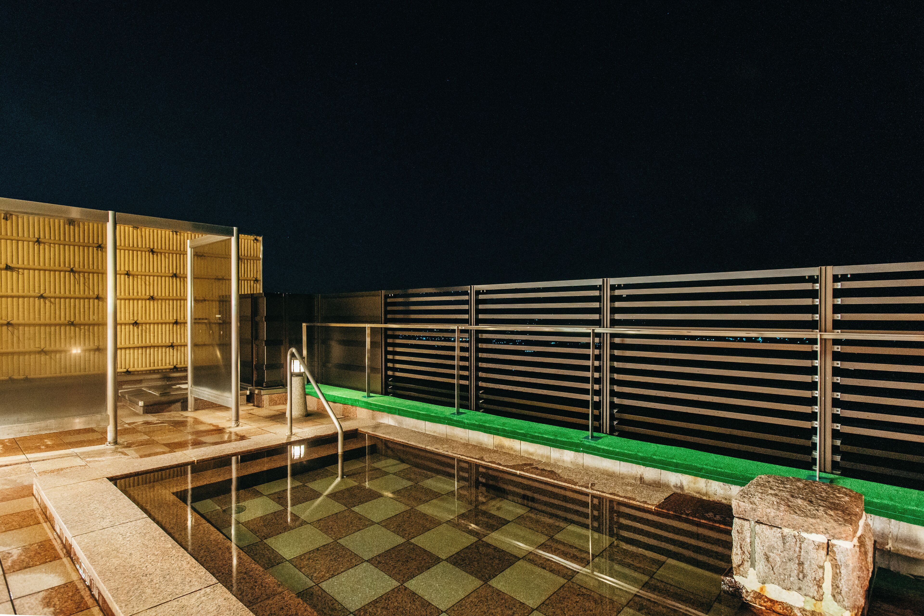 A rooftop pool area with a checkered floor, a green edge, and a stone feature.